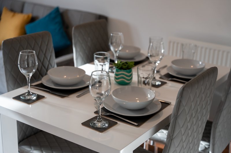 Formal dining table set with place settings, glasses, and gray upholstered chairs