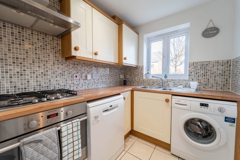 Modern kitchen with cream cabinets, mosaic tile backsplash, stainless steel appliances and washing machine