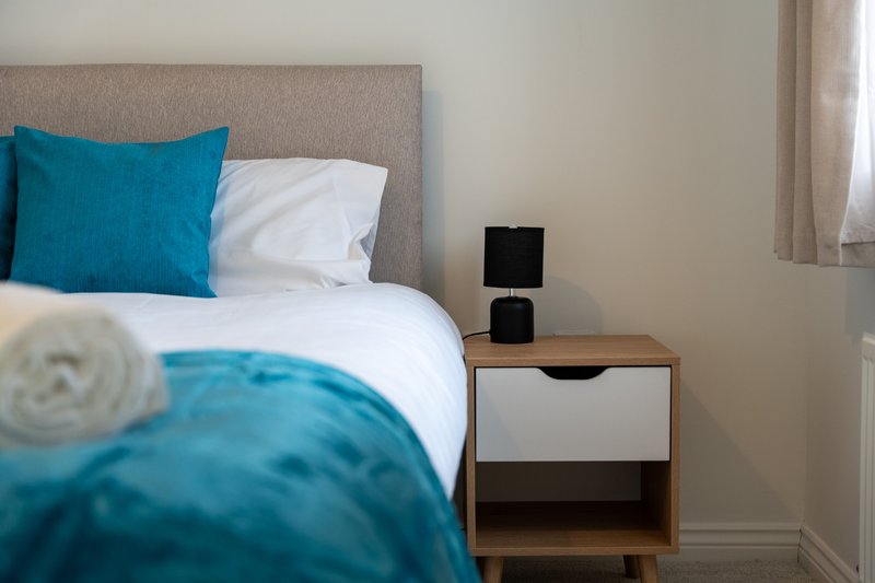 Modern bedroom with teal bedding, gray headboard, wooden nightstand and window