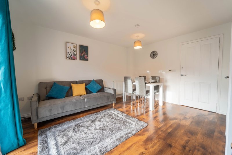 Living room with gray sofa, colorful cushions, dining table, wooden floors and pendant lights