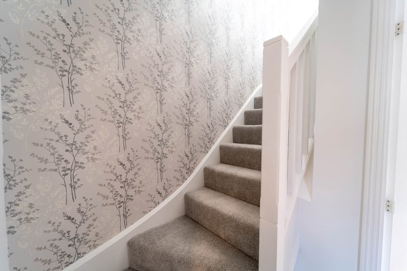 Staircase with carpet treads, white bannister and botanical patterned wallpaper