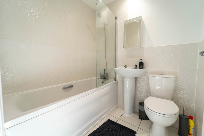 Clean bathroom with bathtub, shower screen, pedestal sink and toilet
