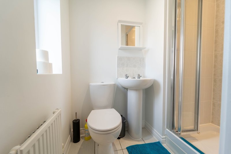 Clean bathroom with white toilet, pedestal sink, mirror, and shower enclosure