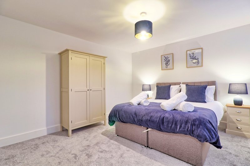 Modern bedroom with double bed, purple bedding, wooden wardrobe, carpet flooring and ceiling light