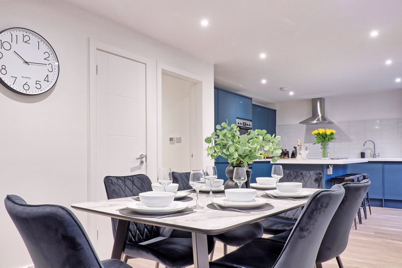 Modern open-plan kitchen and dining area with white table, dark chairs, and blue cabinetry