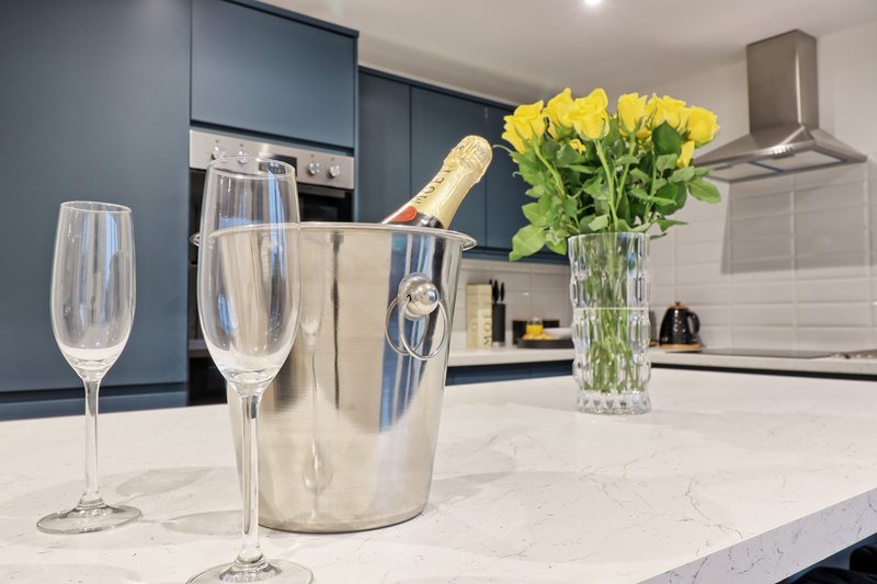 Modern kitchen with champagne bottle in ice bucket, glasses, and yellow flowers on marble countertop