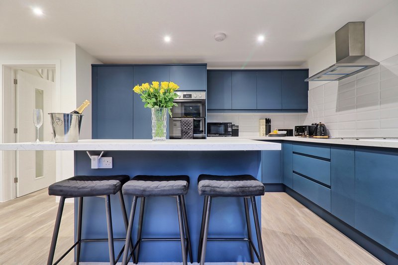 Modern kitchen with blue cabinetry, island with three bar stools, and yellow flowers in vase