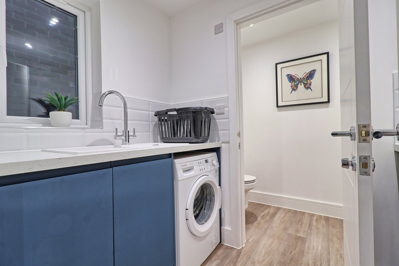 Modern laundry room with blue cabinetry, white sink, washing machine and butterfly artwork