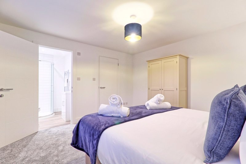 Bright modern bedroom with double bed, purple bedding, wardrobe and ensuite bathroom door