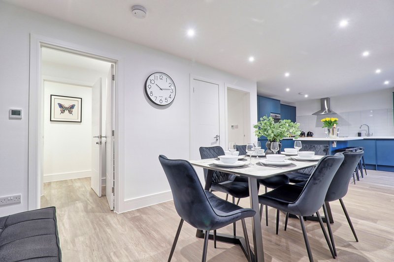 Open-plan dining and kitchen area with white table, black chairs, wall clock and blue cabinetry