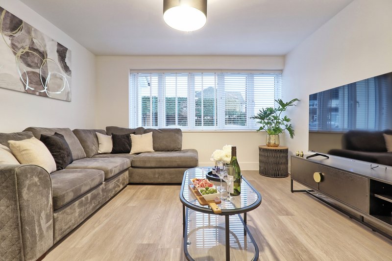 Modern living room with grey corner sofa, coffee table, TV, and large windows overlooking garden