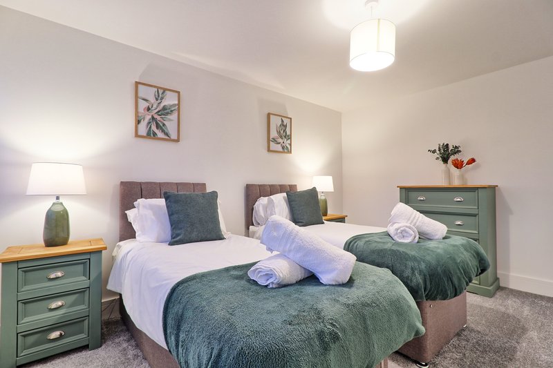 Bedroom with two twin beds, green nightstands, white bedding and rolled towels