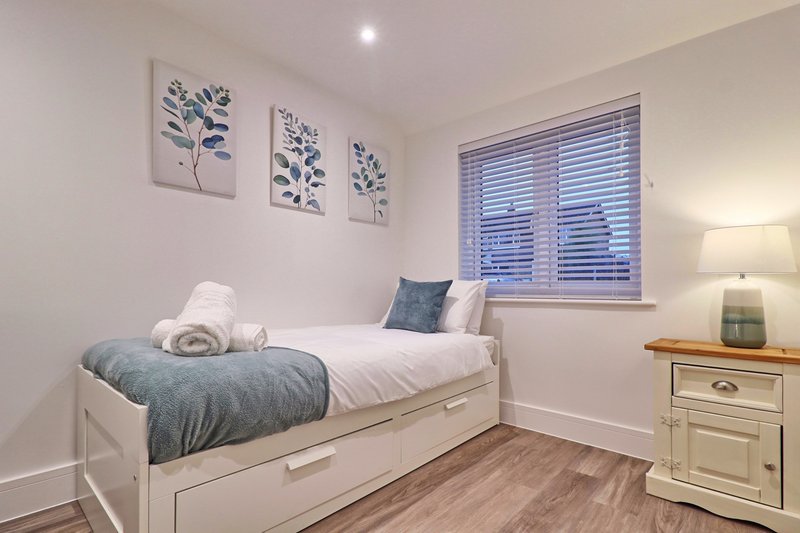Bright bedroom with single bed, white bedding, botanical wall art and wooden flooring