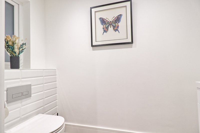Clean bathroom with white toilet, framed butterfly artwork, and vase with dried flowers