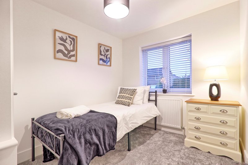 Bedroom with single bed, cream dresser, framed wall art and window with blinds