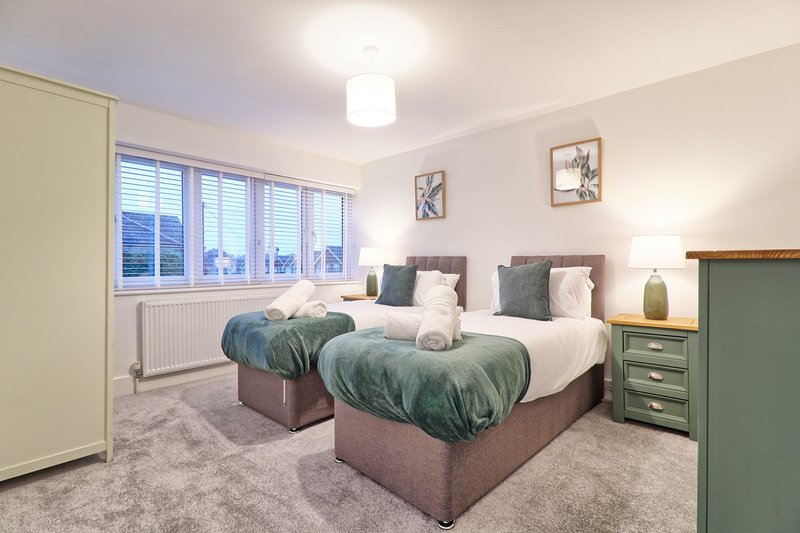 Twin bedroom with two single beds, green bedding, wooden nightstands, and large window