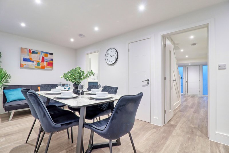 Modern dining area with white table, dark chairs, potted plants and colorful wall art