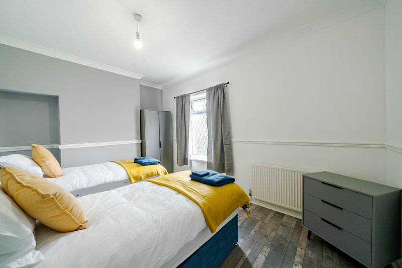 Bright bedroom with two single beds, yellow bedding, dark chest of drawers and window with curtains