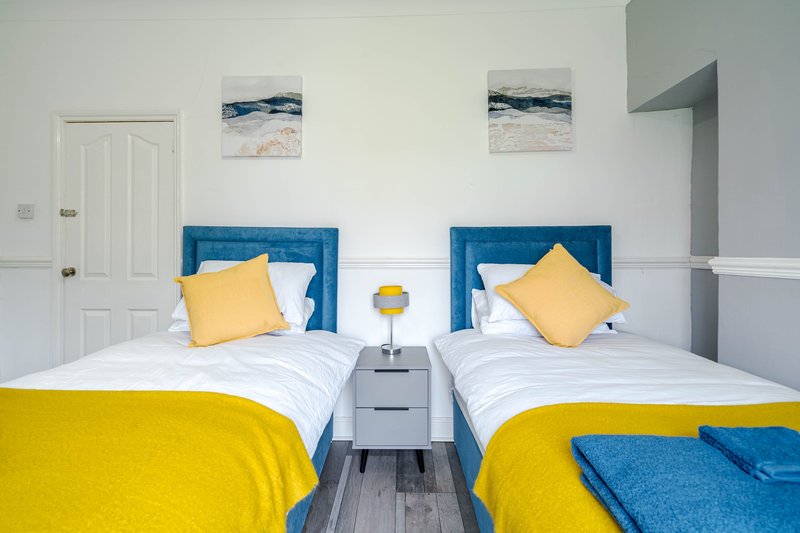Twin bedroom with blue headboards, yellow bedding, yellow cushions, and beach artwork on walls