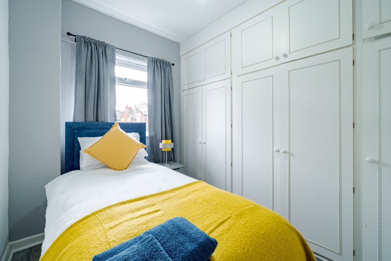Bright bedroom with single bed, yellow bedding, blue headboard and built-in white wardrobes