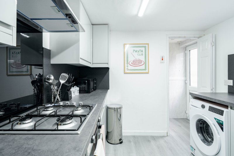 Modern kitchen with black splashback, gas hob, white units and washing machine visible
