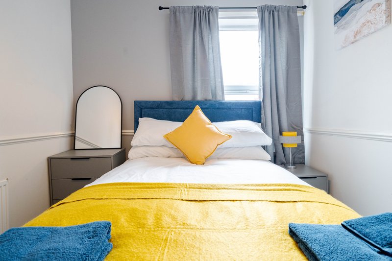 Bright bedroom with yellow bedding, blue headboard, round mirror and grey curtains