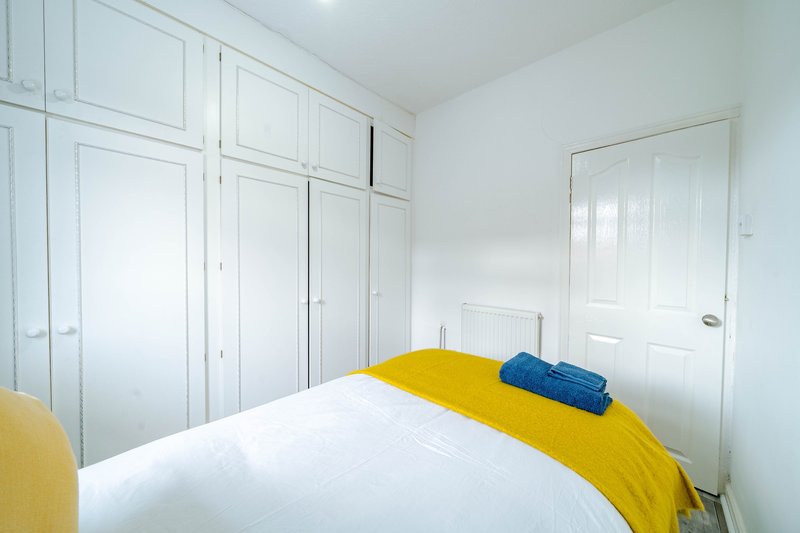 Bright bedroom with double bed, yellow bedding, white fitted wardrobes and door