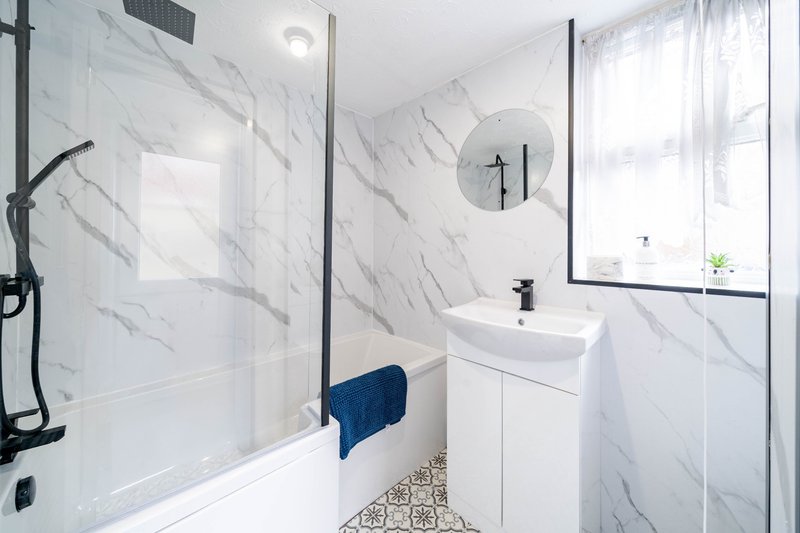 Modern bathroom with marble-effect tiling, glass shower enclosure, white vanity sink and circular mirror