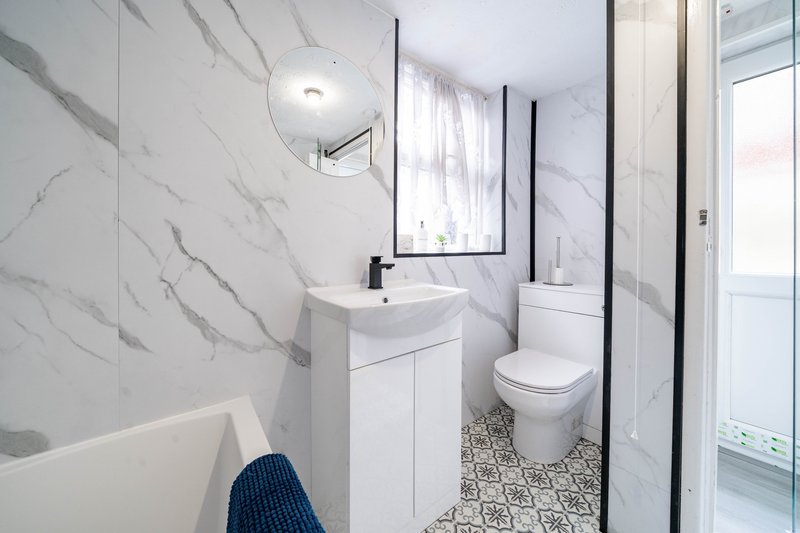 Modern bathroom with marble-effect walls, white vanity, toilet, and patterned floor tiles