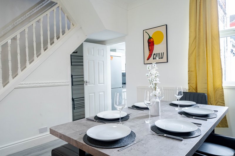 Dining table set for four with white plates, staircase visible, yellow curtains and framed artwork on wall