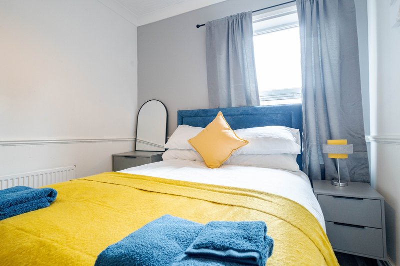 Bright modern bedroom with yellow bedding, blue headboard, white pillows and blue curtains