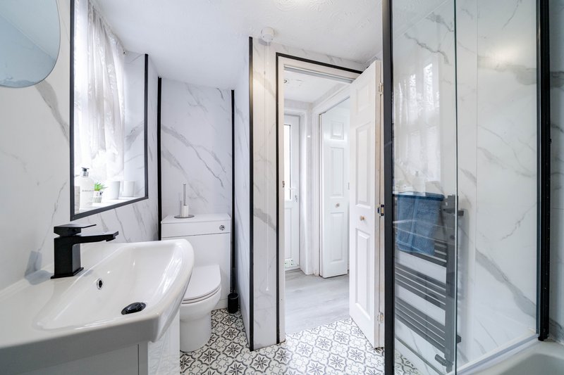 Modern bathroom with white sink, black fixtures, marble tiles, shower enclosure and heated towel rail