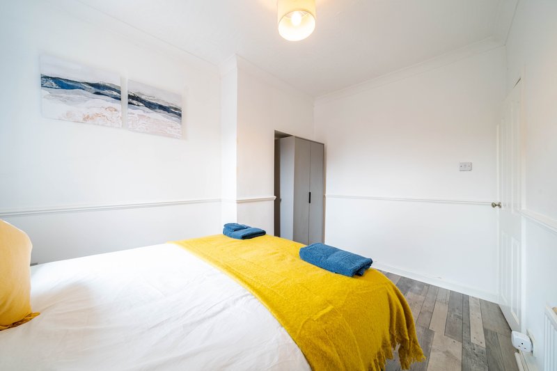 Bedroom with double bed, yellow bedding, blue cushions, coastal wall art, and wooden floor