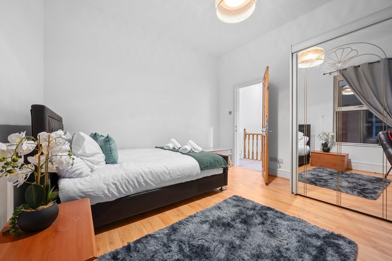Bright bedroom with black bed, wooden floor, large mirror, and potted flowers on nightstand