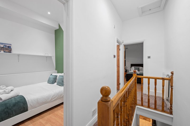 Hallway with wooden staircase railing, white walls, and view into bedroom with white bedding