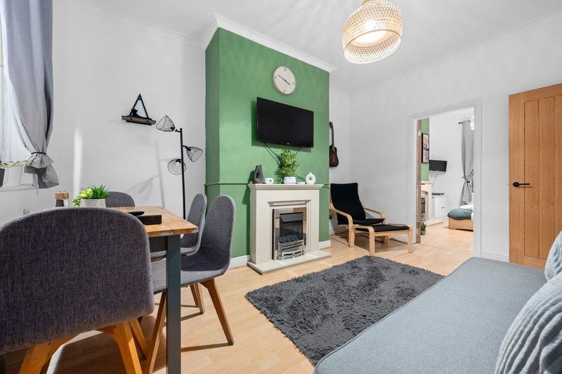 Studio apartment with green accent wall, fireplace, desk area, and bed with grey rug