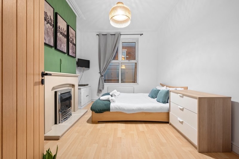 Modern bedroom with single bed, wooden floor, fireplace, and green accent wall