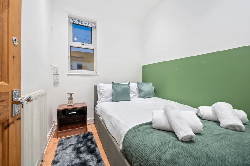 Bedroom with green headboard, double bed, white pillows, wooden nightstand and small window.