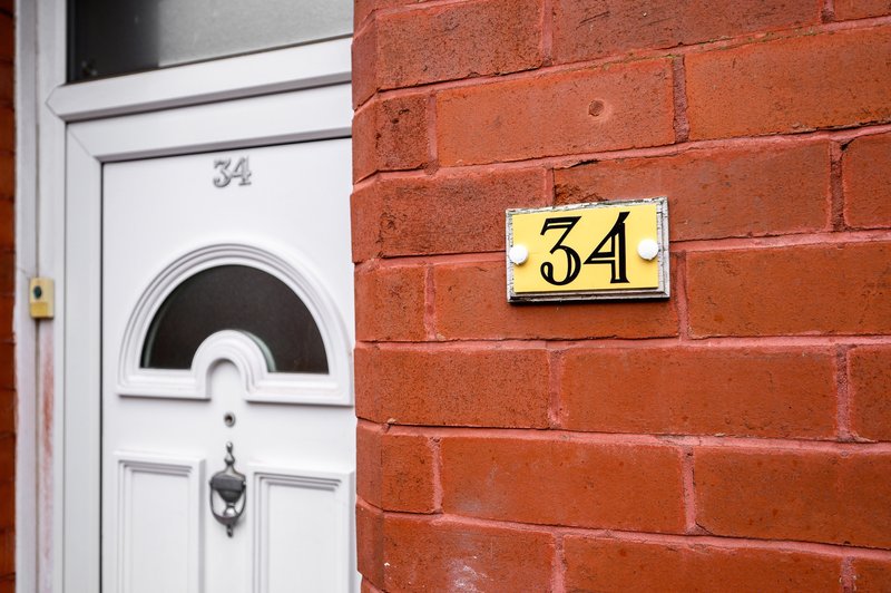 Red brick exterior with white door and yellow house number 34 sign