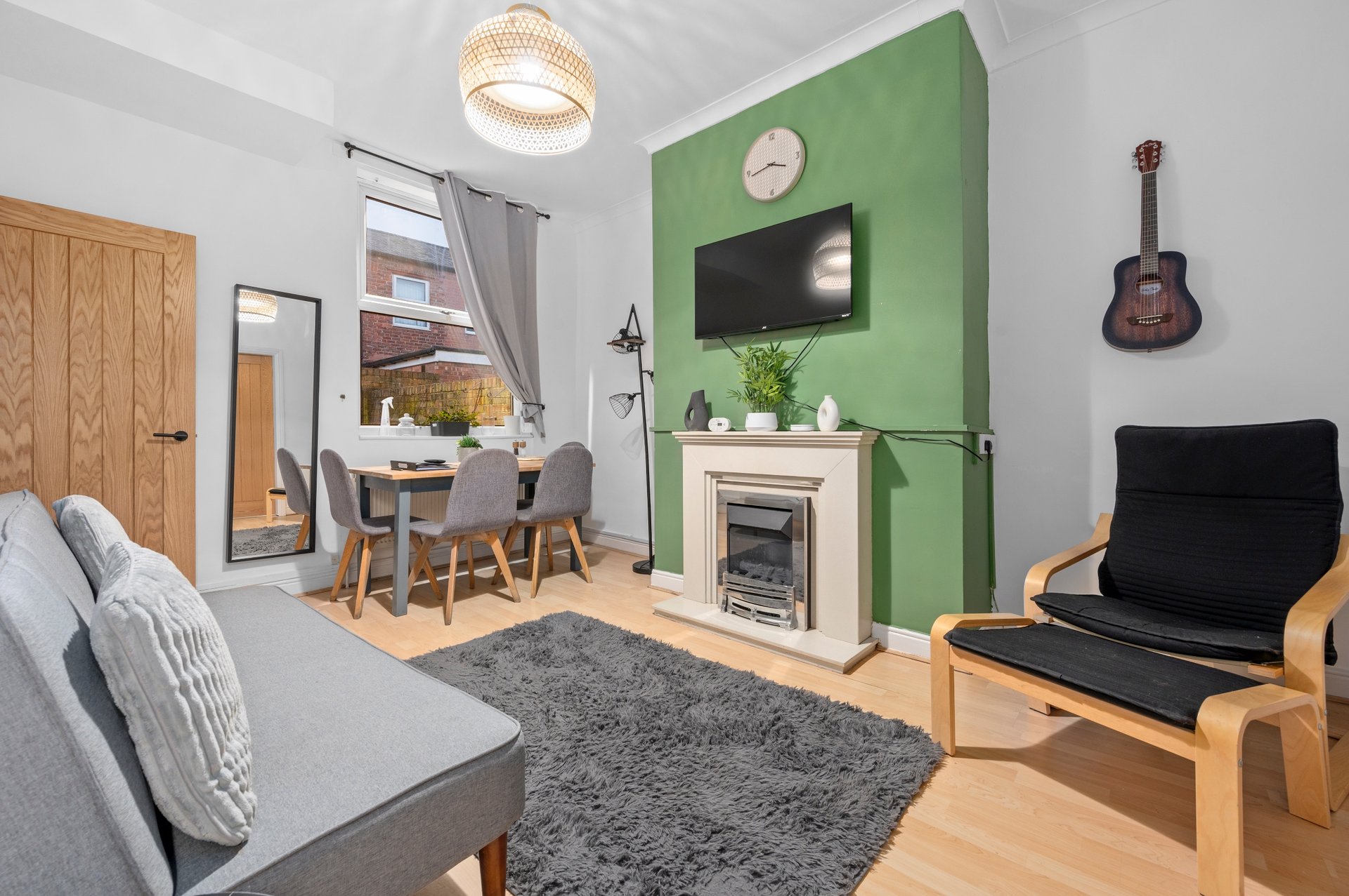 Open-plan living room with sofa, dining area, fireplace, guitar and wooden furniture