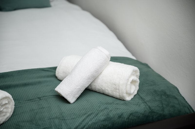 Rolled white towels arranged on green bedding with white pillows