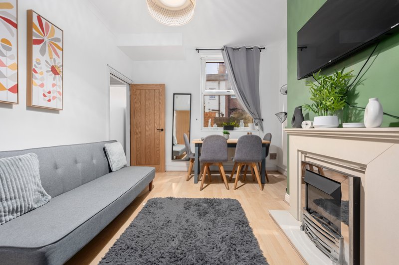 Open-plan living room with gray sofa, dining table, fireplace and green accent wall.