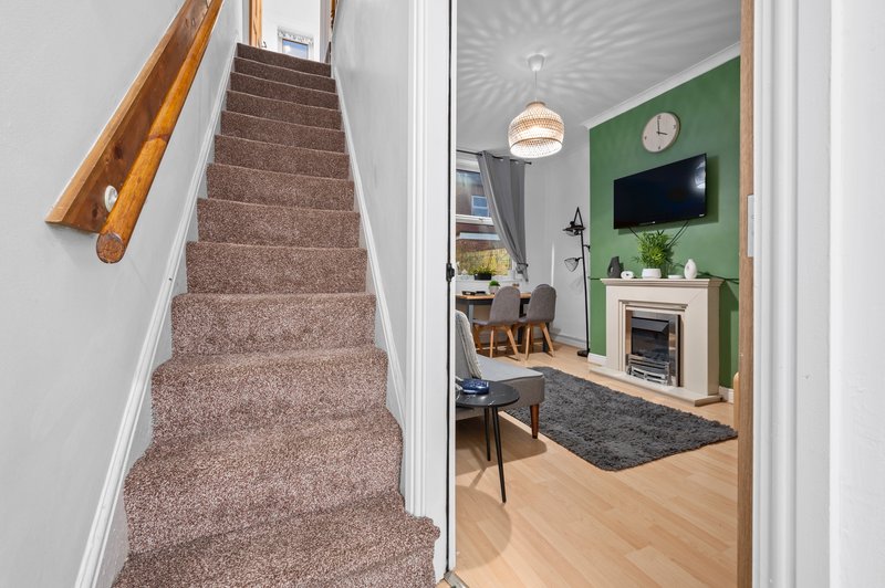 Staircase with brown carpet and wooden handrail opening to green-walled living room with fireplace