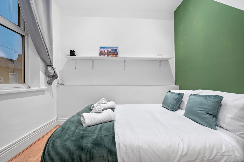 Bright bedroom with double bed, green accent wall, white pillows and folded towels