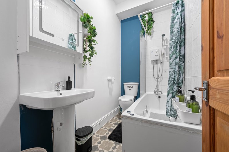 Modern bathroom with white sink, blue accent wall, bathtub and hanging green plants