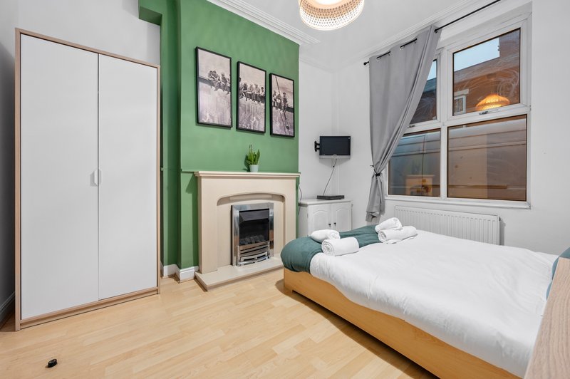 Bright bedroom with green accent wall, fireplace, wooden bed, white wardrobe and window.
