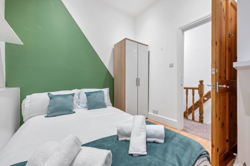 Modern bedroom with double bed, green accent wall, wooden wardrobe and open door