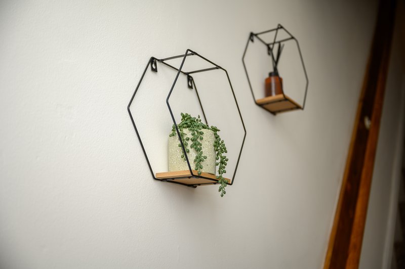 White wall with three geometric wire and wood hanging planters, one containing trailing green plant