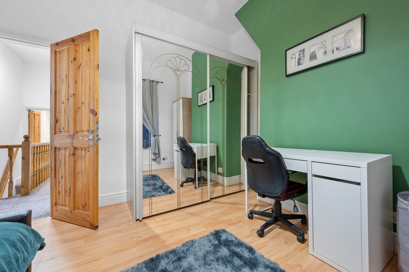 Modern bedroom with green accent wall, wooden doors, desk area and mirrored wardrobe