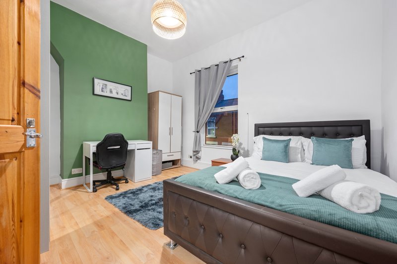 Bedroom with double bed, green accent wall, desk area, wooden flooring and window